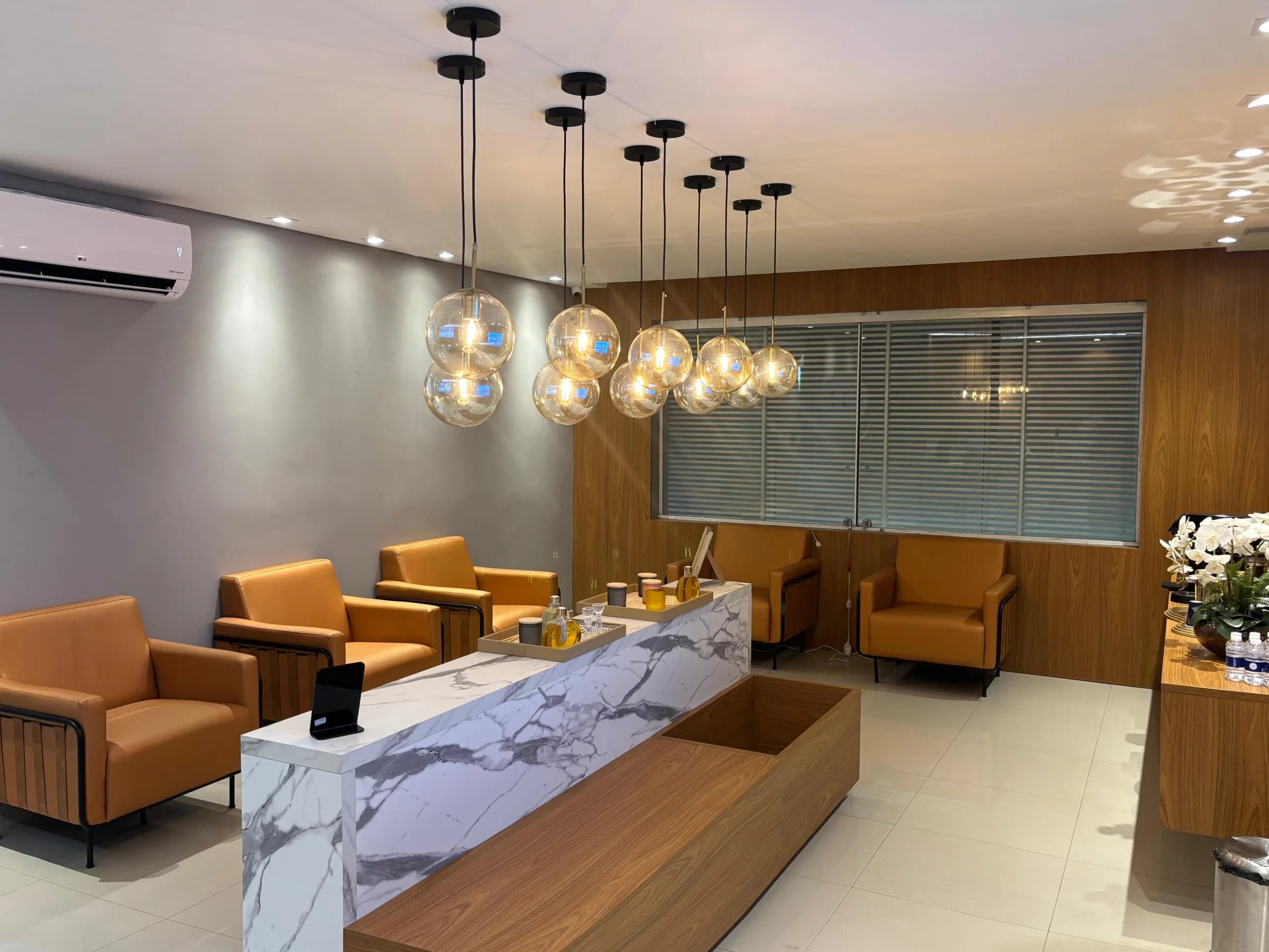 Recepção da Allegra Odontologia com poltronas, balcão em mármore e luminárias suspensas.